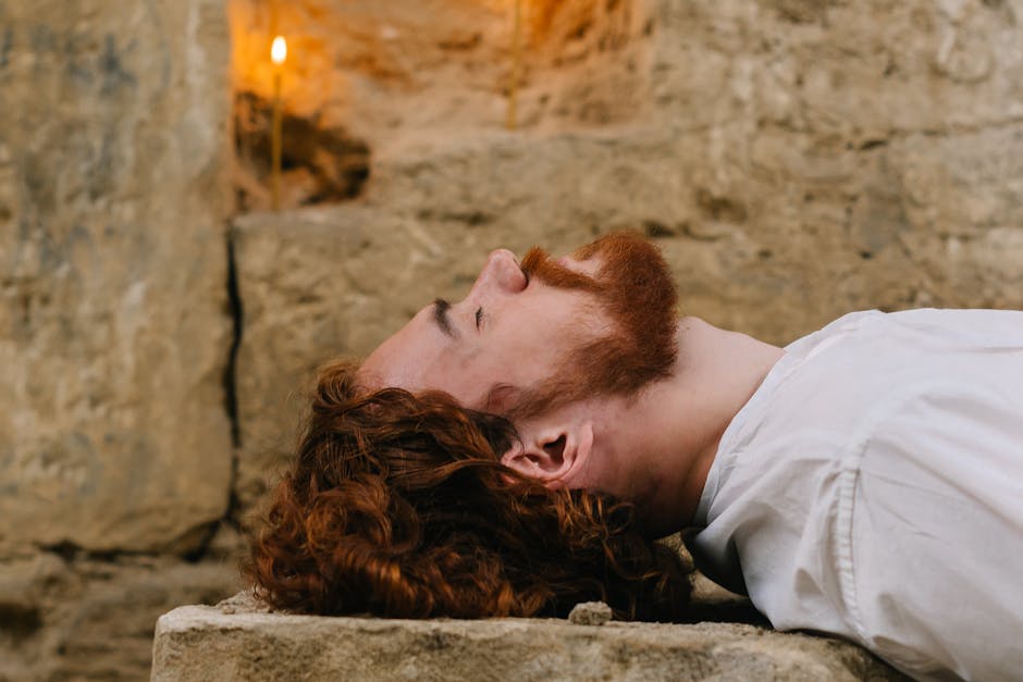 A man with red hair lying down in a candlelit stone setting, evoking calm reflection.