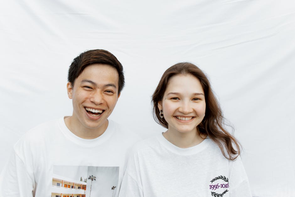 Cheerful couple in white t-shirts smiling against a white background, showcasing joy and happiness.
