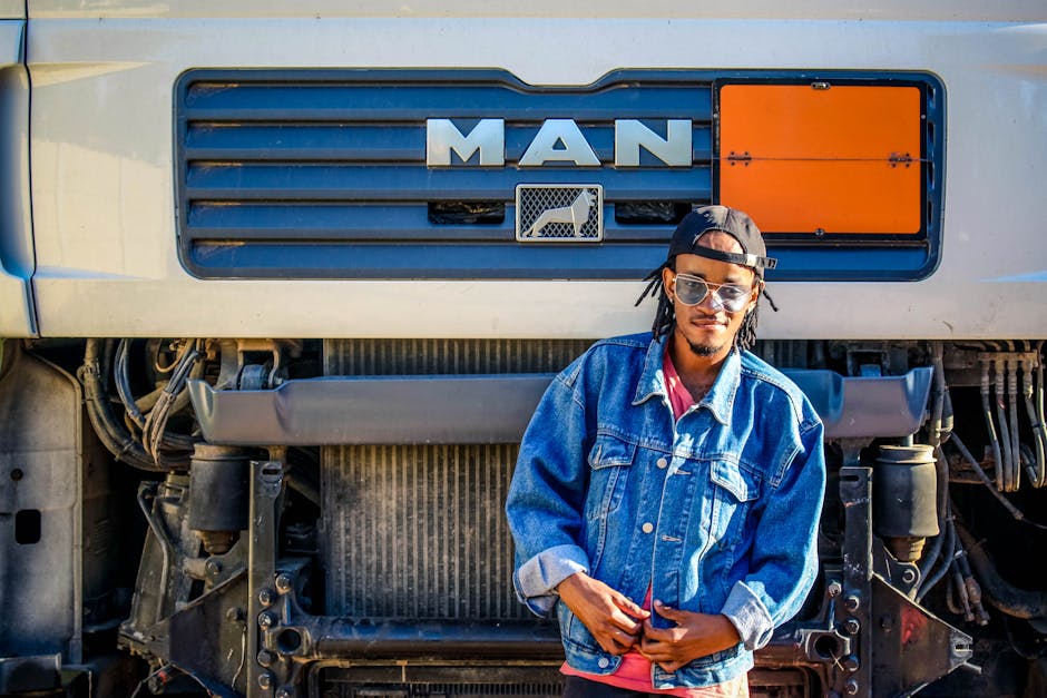 Confident young man in denim jacket poses in front of a MAN truck outdoors. Confident young man in denim jacket poses in front of a MAN truck outdoors.