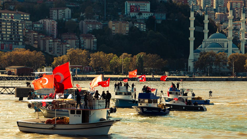Boats adorned with Turkish flags sail on the Bosphorus, with a mosque in the background.