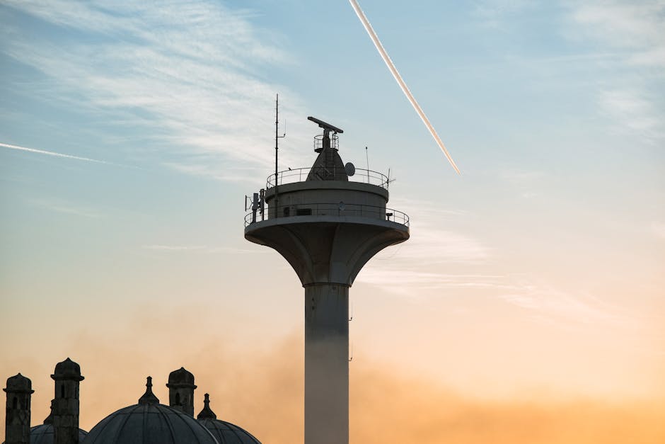 A tall tower silhouetted against a sunset sky with a jet contrail above.