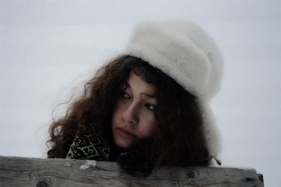 A thoughtful woman in a fur hat gazes into the snowy distance, capturing winter's essence.
