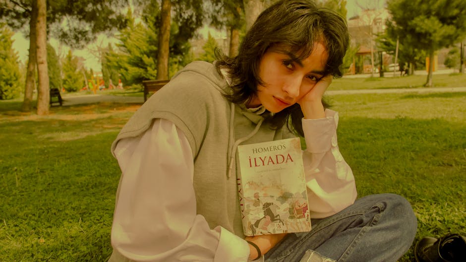 Young woman in a park reading ‘Iliad’ by Homer, enjoying a peaceful outdoor setting. Young woman in a park reading 'Iliad' by Homer, enjoying a peaceful outdoor setting.